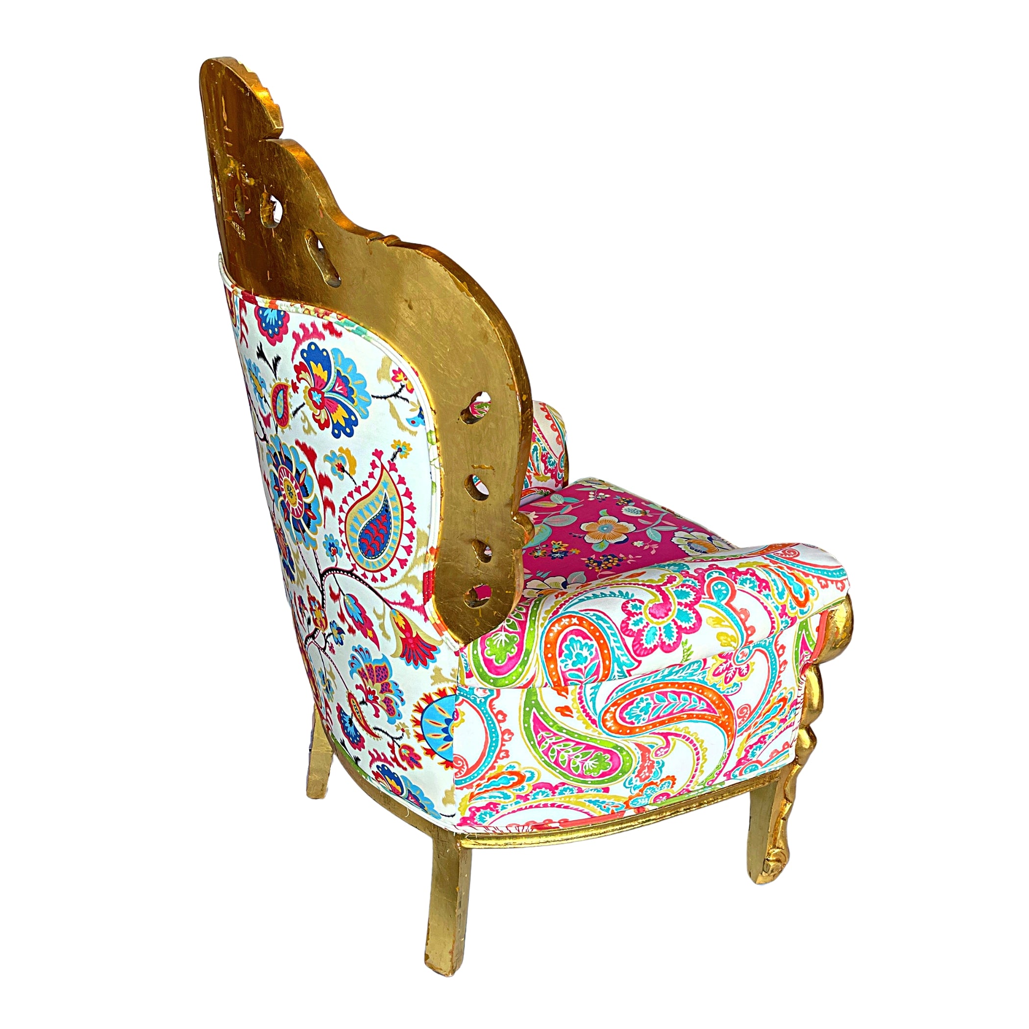 Side view of an ornate baroque armchair with a gold leaf-finished frame and vibrant, multi-colored paisley and floral pattern upholstery, featuring side cut-outs and decorative nailhead trim.