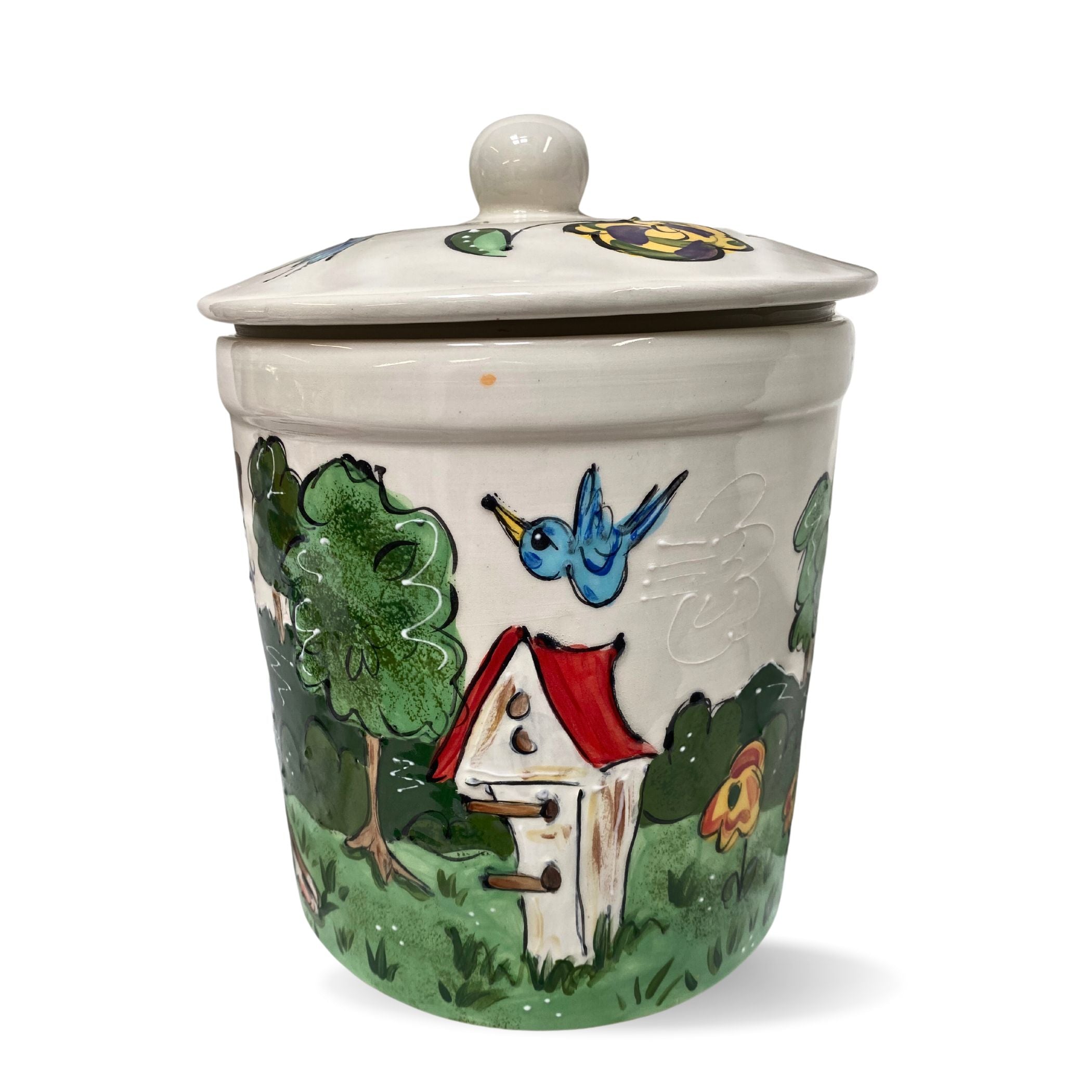 Artisanal ceramic jar with a painting of a blue bird flying towards a red and white birdhouse, surrounded by green bushes and a floral accent