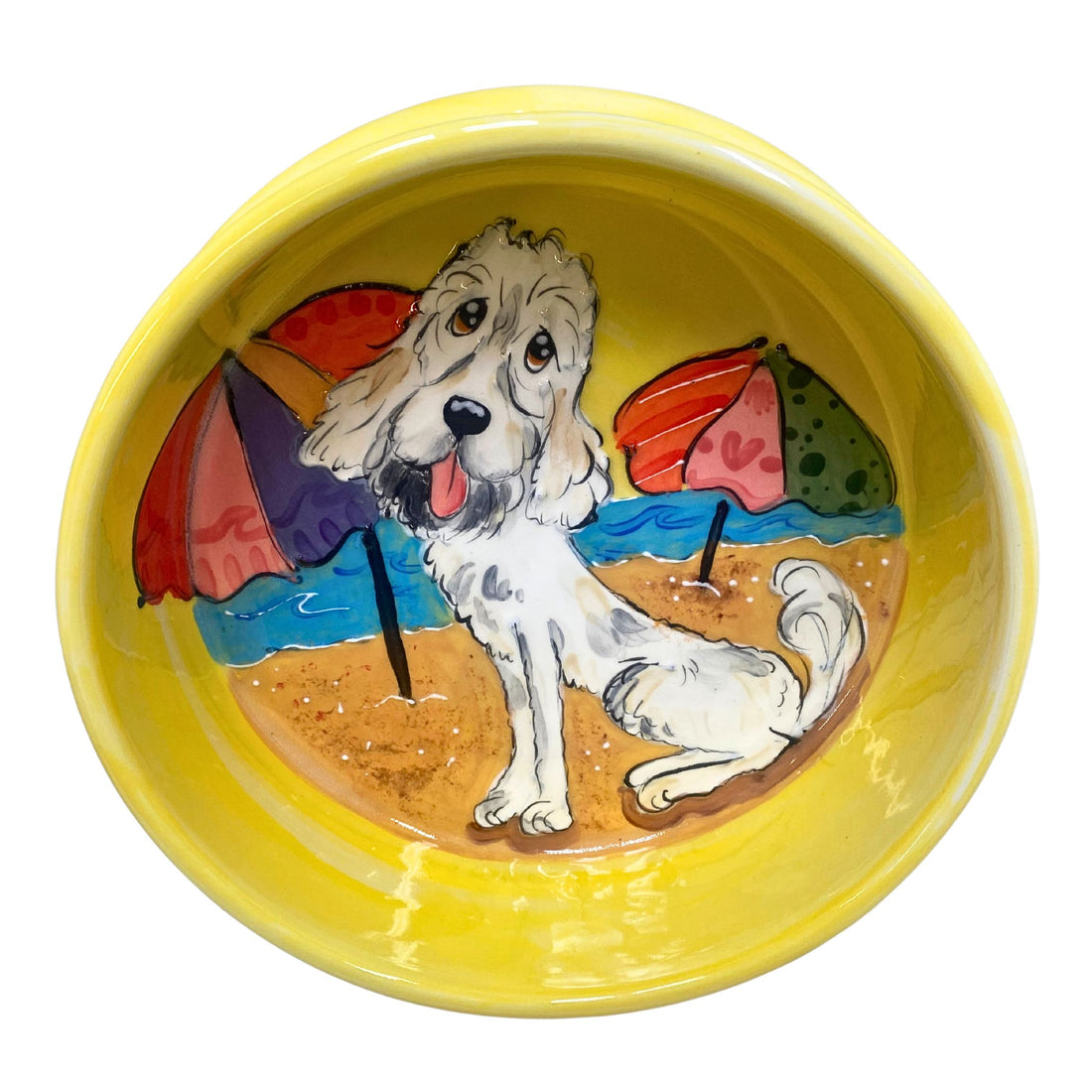 Hand-painted ceramic dog bowl from the &quot;Seaside Companion&quot; Collection, featuring a joyful dog on a sandy beach with colorful beach umbrellas, set against a bright yellow background, capturing the essence of a fun day at the beach