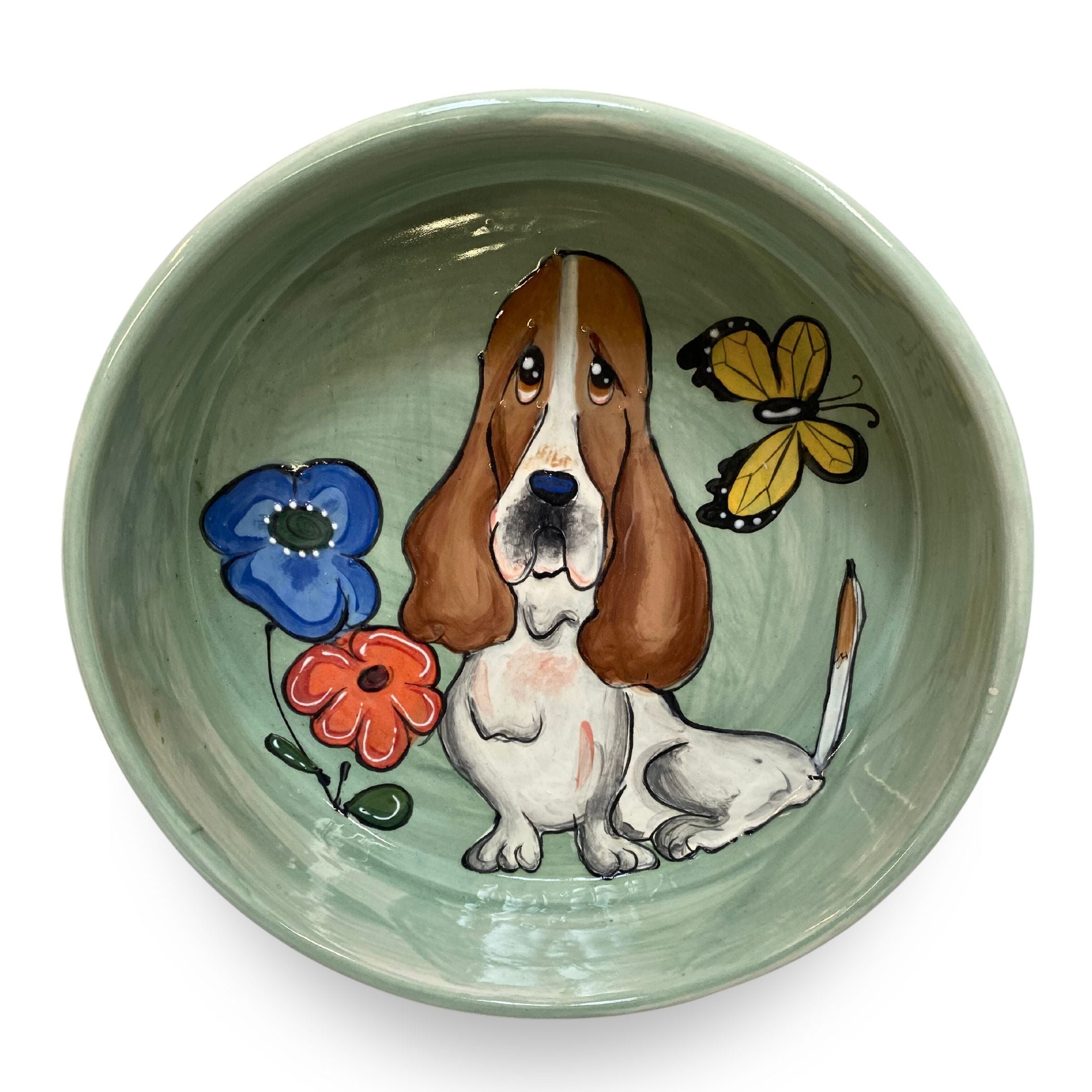 A hand-painted ceramic bowl with a basset hound and butterflies, in calming green hues, capturing a playful and whimsical scene