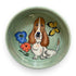 A hand-painted ceramic bowl with a basset hound and butterflies, in calming green hues, capturing a playful and whimsical scene