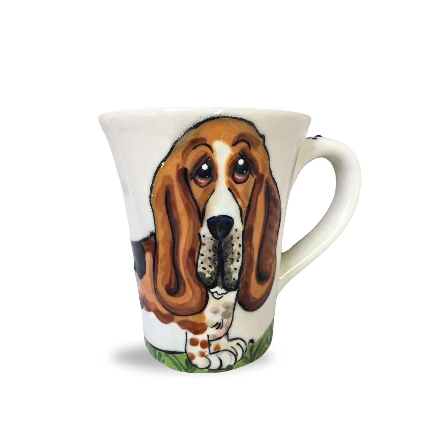 A charming 12 oz coffee mug featuring a hand-painted portrait of a Basset Hound with soulful eyes and long ears, sitting on a grassy field, designed by Debby Carman.