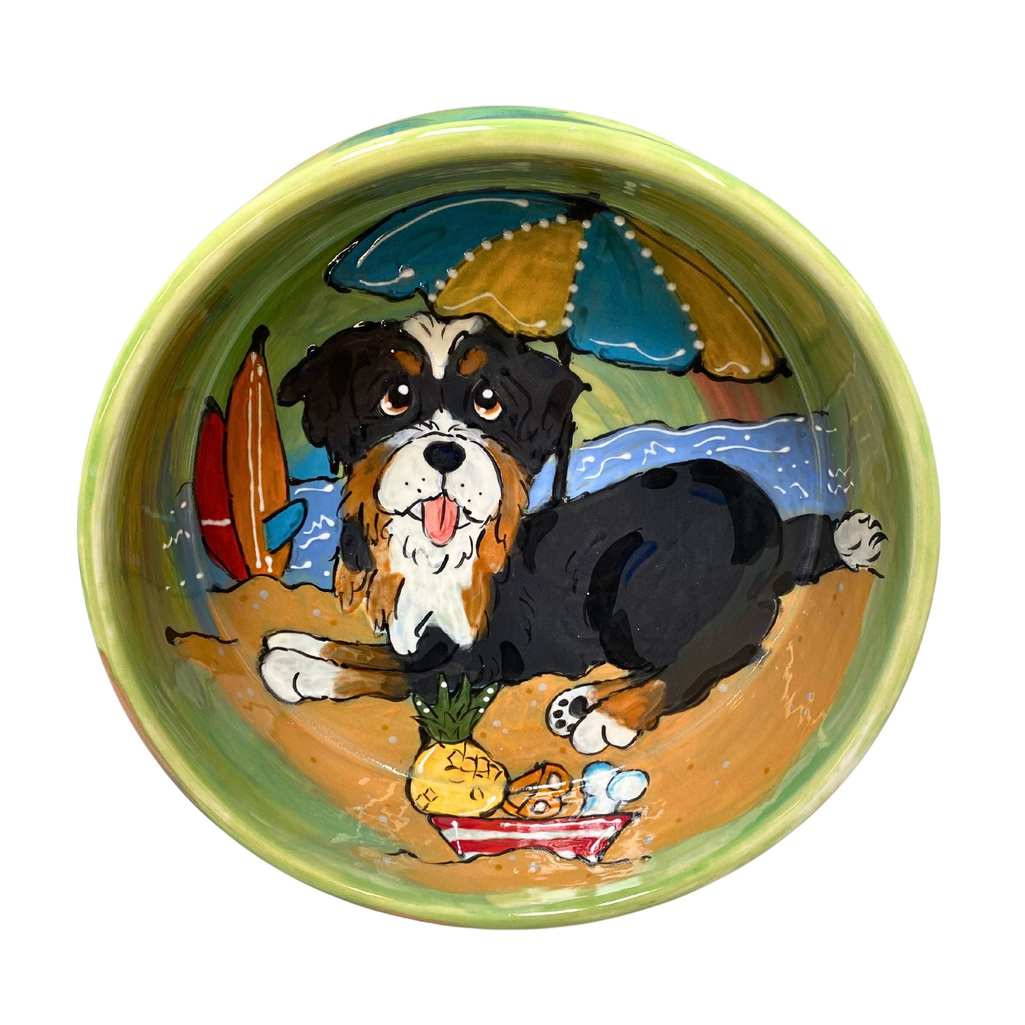 Colorful hand-painted ceramic bowl featuring a playful Bernedoodle dog at a beach picnic scene with surfboards and ocean waves, part of the unique &quot;Canine Coastline&quot; Series for pets