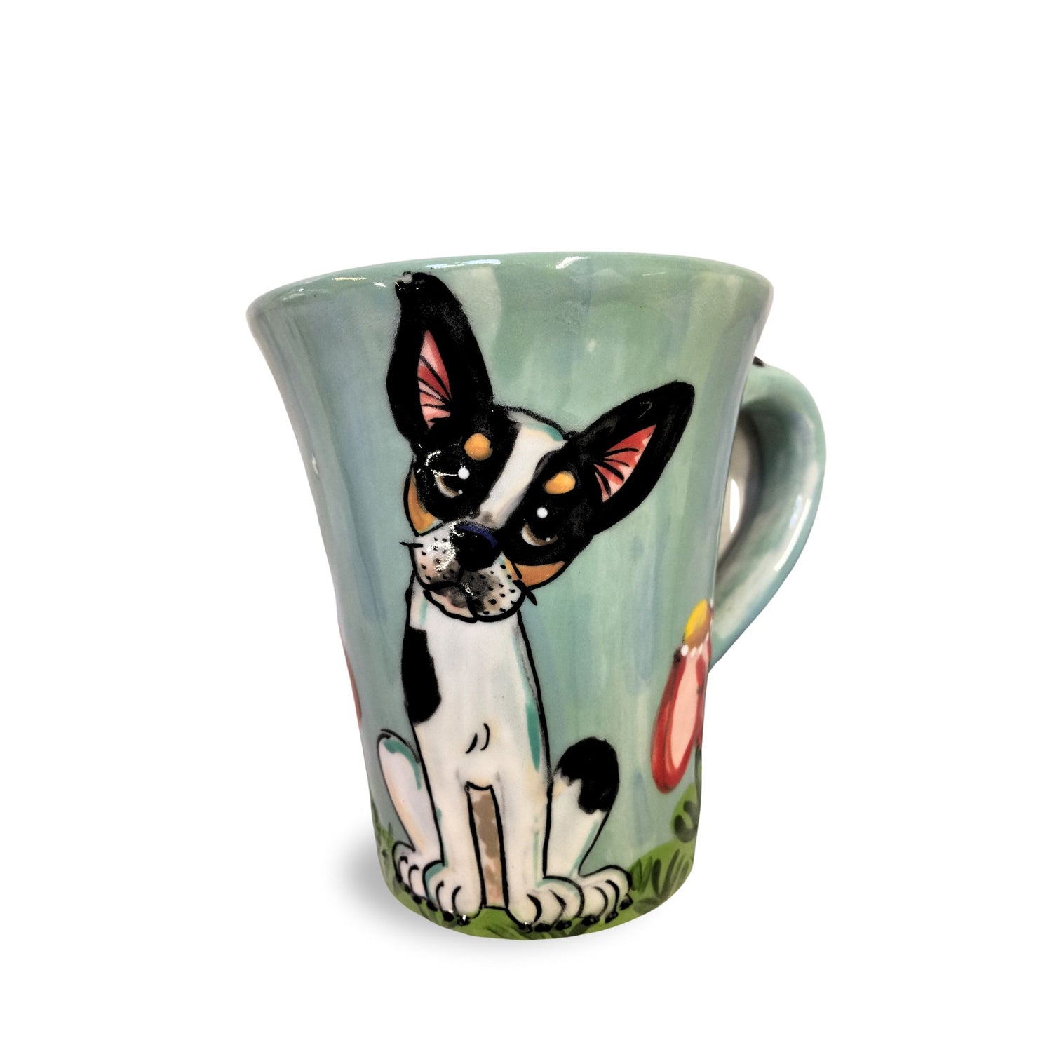 A 12 oz coffee mug with a charming hand-painted Chihuahua seated in a grassy field, with a soft green background and a light blue handle, crafted by Debby Carman.