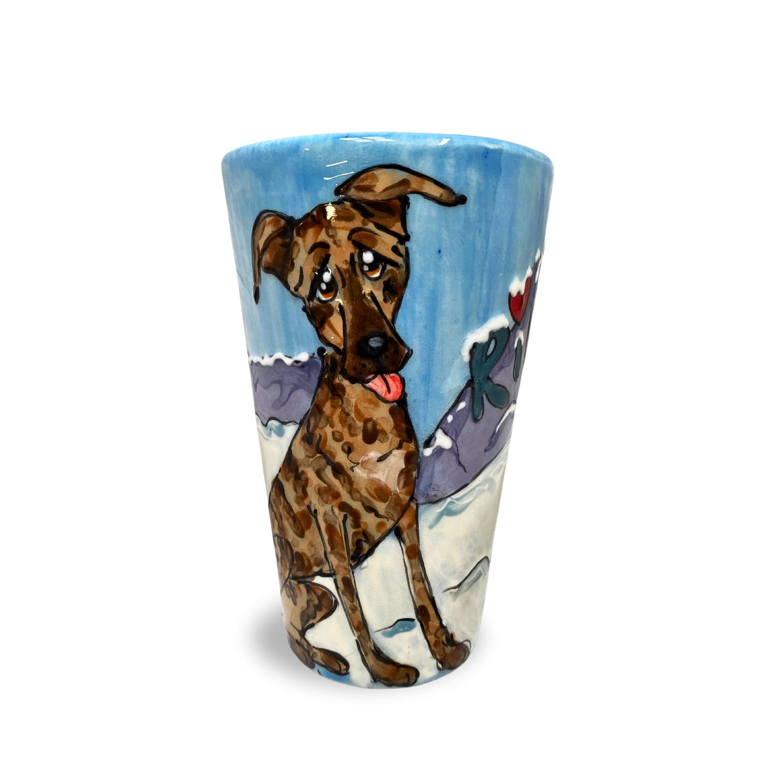 A hand-painted 16 oz tall latte mug with a brindle Great Dane mix dog amidst a whimsical snowy mountain scene, crafted by Debby Carman.