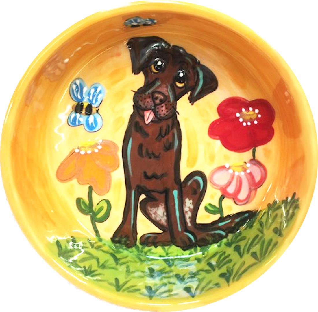 photo of custom ceramic dog bowl with hand painted portrait of chocolate Labrador in garden with flowers and bees on orange bowl handmade by debby carman artist of faux paw productions petique artique