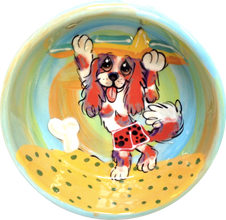 image of cavalier King Charles spaniel taking surfboard to the waves in a sunset beach scene custom created pet bowl hand painted by faux paw productions artist Debby Carman 